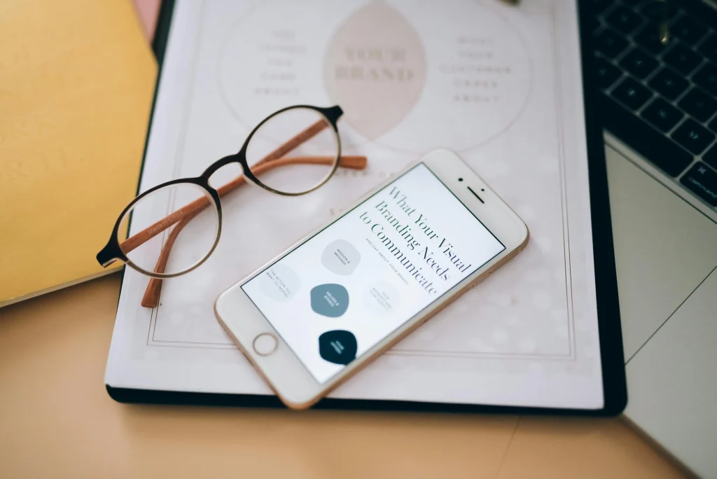 A smartphone displaying branding tips, placed on a desk with glasses, notebook, and laptop, representing influencer marketing strategies.